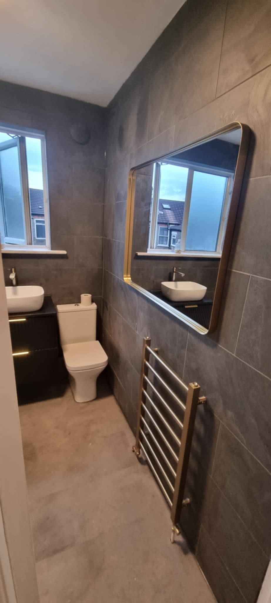 Modern dark bathroom with gold mirror and heated towel rail